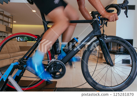 A triathlete riding a triathlon bike on a machine simulation in a modern living room. Training during pandemic conditions. 125281870