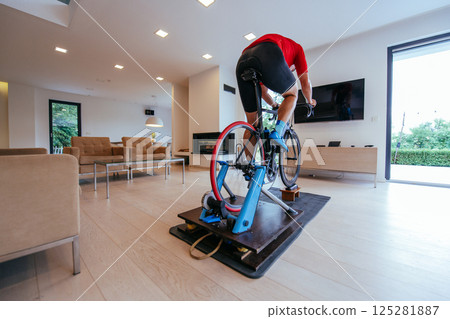 A triathlete riding a triathlon bike on a machine simulation in a modern living room 125281887