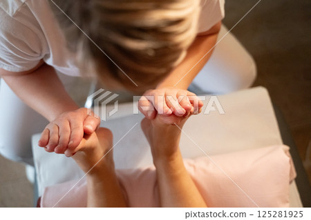 Foot Massage Therapy in a Relaxing Spa Setting. A professional massage therapist in a white uniform provides a soothing foot massage to a client in a calm and serene spa environment Foot Massage Therapy in a Relaxing Spa Setting. A professional massage therapist in a white uniform provides a soothing foot massage to a client in a calm and serene spa environment 125281925