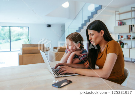 Mother with her daughter talking on laptop with family and friends while sitting in modern living room of big house. 125281937