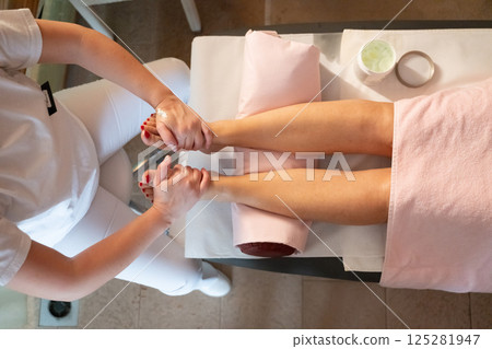 Foot Massage Therapy in a Relaxing Spa Setting. A professional massage therapist in a white uniform provides a soothing foot massage to a client in a calm and serene spa environment 125281947