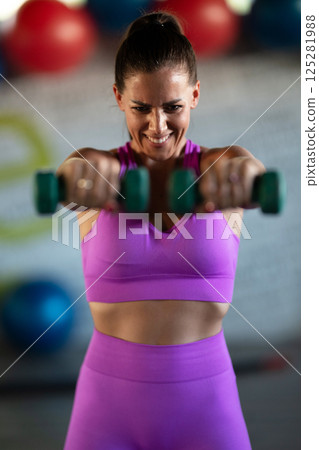 A focused and determined woman performs a strength building dumbbell workout at the gym, showcasing her athletic physique and dedication to fitness. A focused and determined woman performs a strength building dumbbell workout at the gym, showcasing her athletic physique and dedication to fitness. 125281988