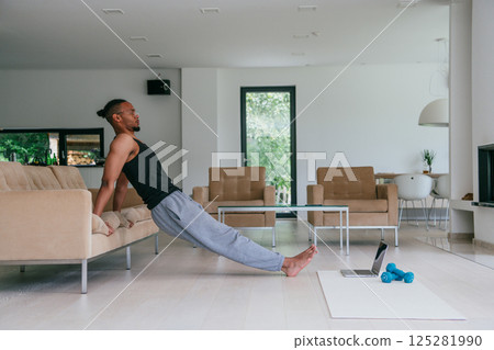 Training At Home. Sporty man doing the training while watching an online tutorial on a laptop, exercising in the living room, free space. Training At Home. Sporty man doing the training while watching an online tutorial on a laptop, exercising in the living room, free space. 125281990