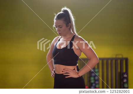 A fit and determined woman takes a short break during an intense workout session at the gym, showcasing strength and perseverance. 125282001