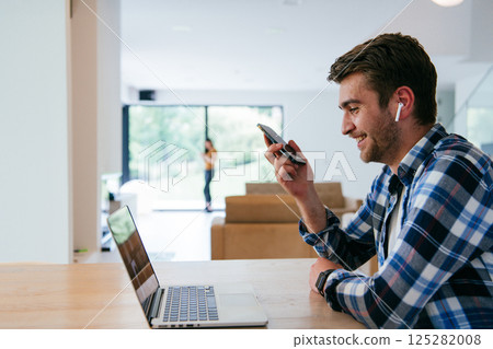 A freelancer sitting at a table in a modern living room, with headphones using a laptop for business video chat, conversation with friends and entertainment A freelancer sitting at a table in a modern living room, with headphones using a laptop for business video chat, conversation with friends and entertainment 125282008