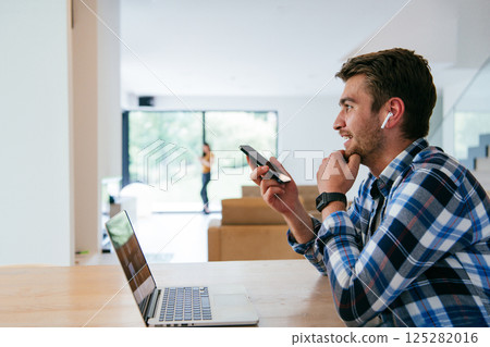 A freelancer sitting at a table in a modern living room, with headphones using a laptop for business video chat, conversation with friends and entertainment A freelancer sitting at a table in a modern living room, with headphones using a laptop for business video chat, conversation with friends and entertainment 125282016