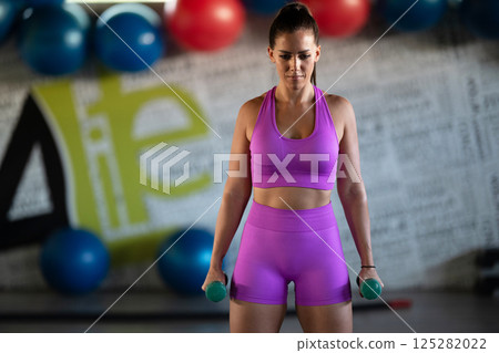 A focused and determined woman performs a strength building dumbbell workout at the gym, showcasing her athletic physique and dedication to fitness. A focused and determined woman performs a strength building dumbbell workout at the gym, showcasing her athletic physique and dedication to fitness. 125282022