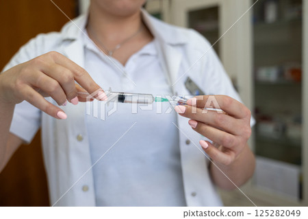 A focused nurse in a white lab coat carefully prepares a syringe for an injection in a professional healthcare environment. A focused nurse in a white lab coat carefully prepares a syringe for an injection in a professional healthcare environment. 125282049