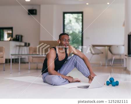 Training At Home. Sporty man doing the training while watching an online tutorial on a laptop, exercising in the living room, free space. Training At Home. Sporty man doing the training while watching an online tutorial on a laptop, exercising in the living room, free space. 125282111