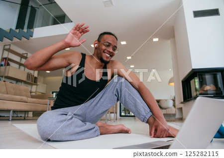 Training At Home. Sporty African American man doing the training while watching an online tutorial on a laptop, exercising in the living room, free space 125282115
