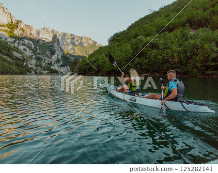 A young couple enjoying an idyllic kayak ride in the middle of a beautiful river surrounded by forest greenery 125282141