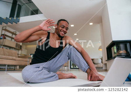 Training At Home. Sporty African American man doing the training while watching an online tutorial on a laptop, exercising in the living room, free space 125282142