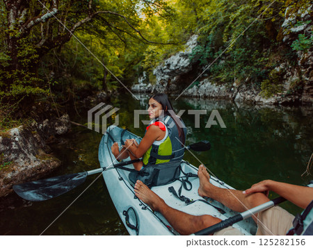 A young couple enjoying an idyllic kayak ride in the middle of a beautiful river surrounded by forest greenery 125282156