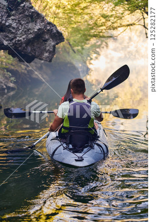 A young couple enjoying an idyllic kayak ride in the middle of a beautiful river surrounded by forest greenery 125282177