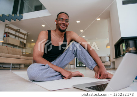 Training At Home. Sporty man doing the training while watching an online tutorial on a laptop, exercising in the living room, free space. 125282178