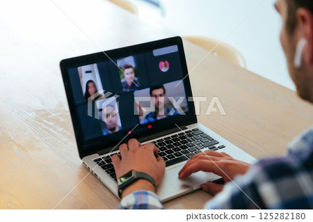 A freelancer sitting at a table in a modern living room, with headphones using a laptop for business video chat, conversation with friends and entertainment 125282180