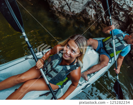A young couple enjoying an idyllic kayak ride in the middle of a beautiful river surrounded by forest greenery 125282234