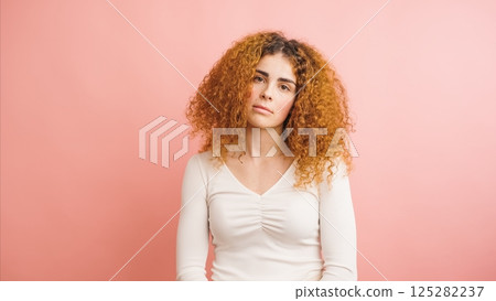 Young woman with frizzy red hair showing confidence against pink background 125282237