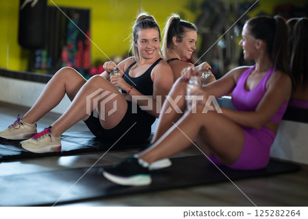 Two fitness women resting and recovering in the gym after an intense workout session, showcasing strength, endurance, and dedication to their fitness journey. Two fitness women resting and recovering in the gym after an intense workout session, showcasing strength, endurance, and dedication to their fitness journey. 125282264