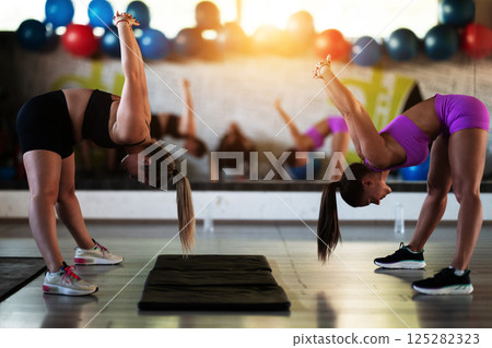 Two fitness women stretch together in the gym, supporting each other in their journey towards flexibility and wellness. 125282323