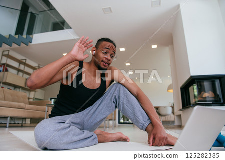 Training At Home. Sporty African American man doing the training while watching an online tutorial on a laptop, exercising in the living room, free space 125282385
