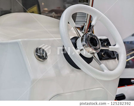 Boat steering wheel console with shiny chrome accents and clean white design showcasing marine equipment and craftsmanship Boat steering wheel console with shiny chrome accents and clean white design showcasing marine equipment and craftsmanship 125282392