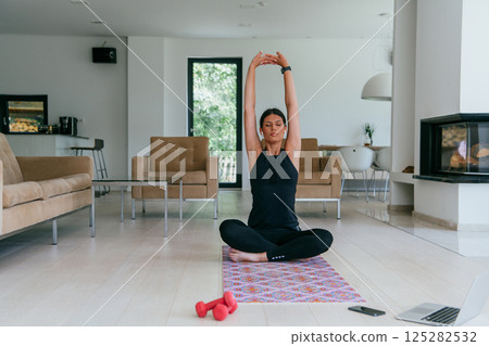 Young Beautiful Female Exercising, Stretching and Practising Yoga with Trainer via Video Call Conference in Bright Sunny House. Healthy Lifestyle, Wellbeing and Mindfulness Concept 125282532