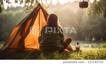Alone with yourself. Back view of a female hiker enjoys a morning cup of coffee near her tent, alone with nature. The breath of the morning foggy forest and the spirit of freedom. Vertical photo. 125282533