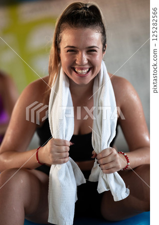 A beautiful and fit woman sitting on a gym ball with a towel, resting and recovering after an intense workout. 125282566