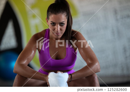 A beautiful and fit woman sitting on a gym ball with a towel, resting and recovering after an intense workout. A beautiful and fit woman sitting on a gym ball with a towel, resting and recovering after an intense workout. 125282600