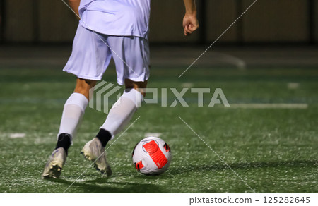 Soccer Player in White Uniform Dribbling Soccer Ball on Field at Night Soccer Player in White Uniform Dribbling Soccer Ball on Field at Night 125282645