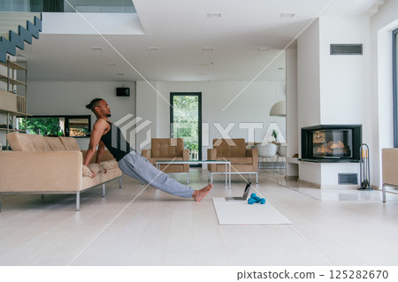 Training At Home. Sporty man doing the training while watching an online tutorial on a laptop, exercising in the living room, free space. Training At Home. Sporty man doing the training while watching an online tutorial on a laptop, exercising in the living room, free space. 125282670