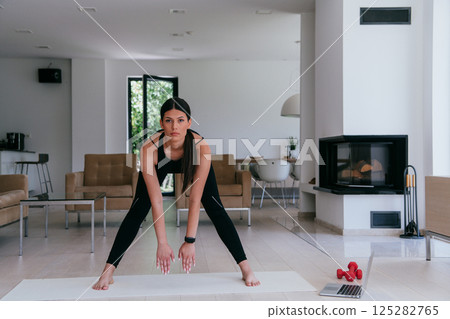 Young Beautiful Female Exercising, Stretching and Practising Yoga with Trainer via Video Call Conference in Bright Sunny House. Healthy Lifestyle, Wellbeing and Mindfulness Concept Young Beautiful Female Exercising, Stretching and Practising Yoga with Trainer via Video Call Conference in Bright Sunny House. Healthy Lifestyle, Wellbeing and Mindfulness Concept 125282765