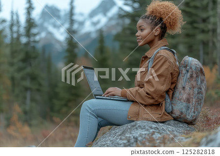 Woman during hike sitting on a rock with a laptop on her lap. Remote work. A young woman finds tranquility on a rock, using her laptop to complete freelance work in nature. 125282818