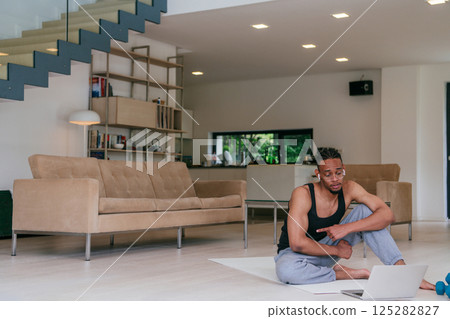 Training At Home. Sporty African American man doing the training while watching an online tutorial on a laptop, exercising in the living room, free space 125282827