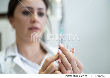A focused nurse in a white lab coat carefully prepares a syringe for an injection in a professional healthcare environment. A focused nurse in a white lab coat carefully prepares a syringe for an injection in a professional healthcare environment. 125282829