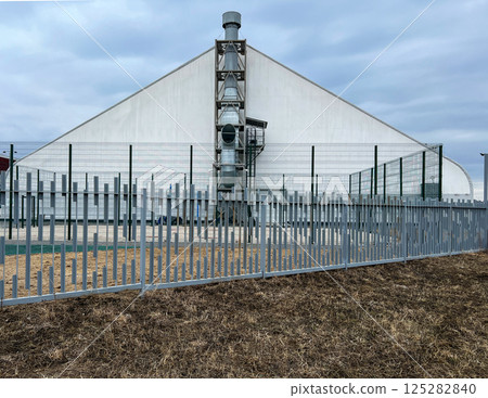 Industrial building with large ventilation system enclosed by a metal fence, set against a cloudy sky. Architecture showing functional and protective design elements Industrial building with large ventilation system enclosed by a metal fence, set against a cloudy sky. Architecture showing functional and protective design elements 125282840