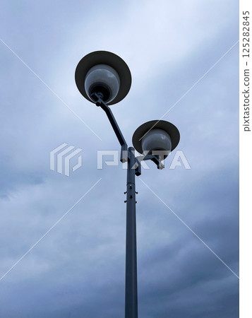 minimalist photo of modern street lamp with two globe-shaped lights, set against an overcast sky, emphasizes the simplicity and functionality of urban design 125282845