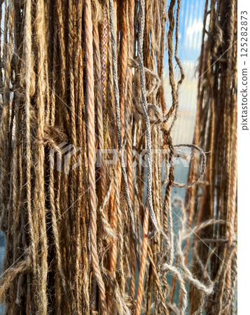 detailed view of natural fiber threads hanging close together, showcasing their varied textures and colors under sunlight. Highlights the organic and rustic appeal of raw fibers detailed view of natural fiber threads hanging close together, showcasing their varied textures and colors under sunlight. Highlights the organic and rustic appeal of raw fibers 125282873