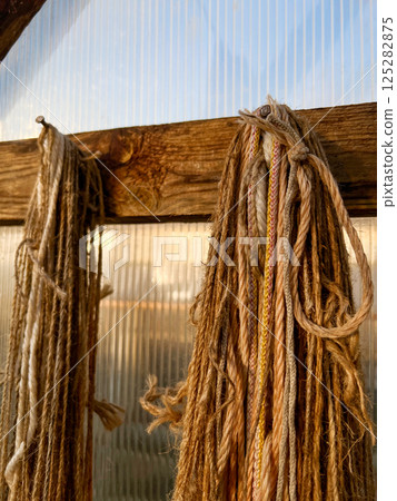 Natural fiber ropes in various textures and colors hang neatly from a wooden beam in a workshop setting, creating an artisanal and rustic atmosphere Natural fiber ropes in various textures and colors hang neatly from a wooden beam in a workshop setting, creating an artisanal and rustic atmosphere 125282875
