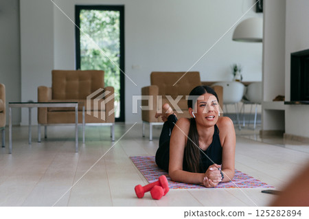 Young woman resting after online training while lying on the living room floor. 125282894