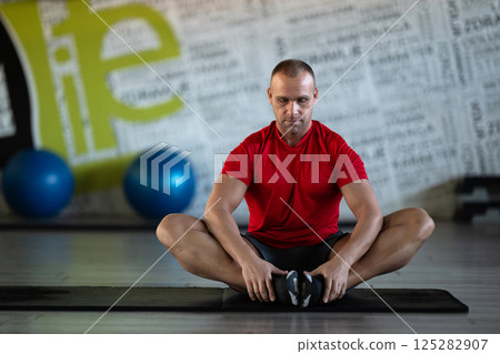 A fitness man stretches in the gym after an intense workout, focusing on recovery and flexibility. 125282907