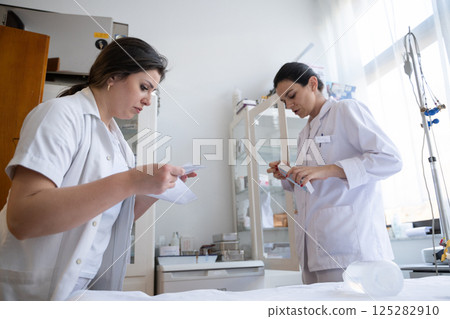 Two nurses in a hospital laboratory are carefully inspecting and preparing medications for patients and hospital use. 125282910