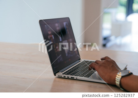 Photo of a laptop with modern headphones on a wooden table in a house with a modern interior.  125282937