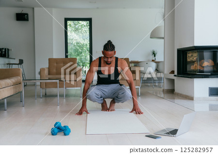 Training At Home. Sporty african american man doing the training while watching an online tutorial on a laptop, exercising in the living room, free space. Training At Home. Sporty african american man doing the training while watching an online tutorial on a laptop, exercising in the living room, free space. 125282957