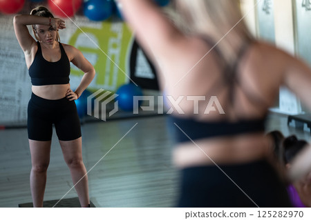 A fit and determined woman takes a short break during an intense workout session at the gym, showcasing strength and perseverance. A fit and determined woman takes a short break during an intense workout session at the gym, showcasing strength and perseverance. 125282970