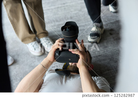 A photographer lies on the floor, capturing a heartfelt shot of a group of models embracing each other, showcasing their natural connection and joy in an intimate and creative moment 125282987