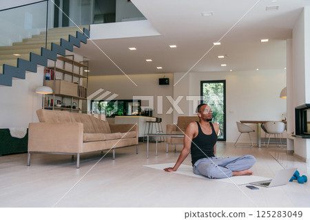 Training At Home. Sporty African American man doing the training while watching an online tutorial on a laptop, exercising in the living room, free space Training At Home. Sporty African American man doing the training while watching an online tutorial on a laptop, exercising in the living room, free space 125283049