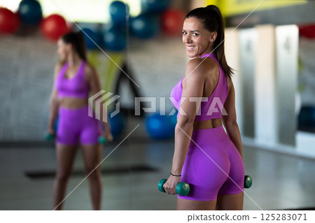 A focused and determined woman performs a strength building dumbbell workout at the gym, showcasing her athletic physique and dedication to fitness. A focused and determined woman performs a strength building dumbbell workout at the gym, showcasing her athletic physique and dedication to fitness. 125283071
