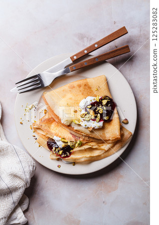 Breakfast crepes with sour cream, jam and pistachio. 125283082